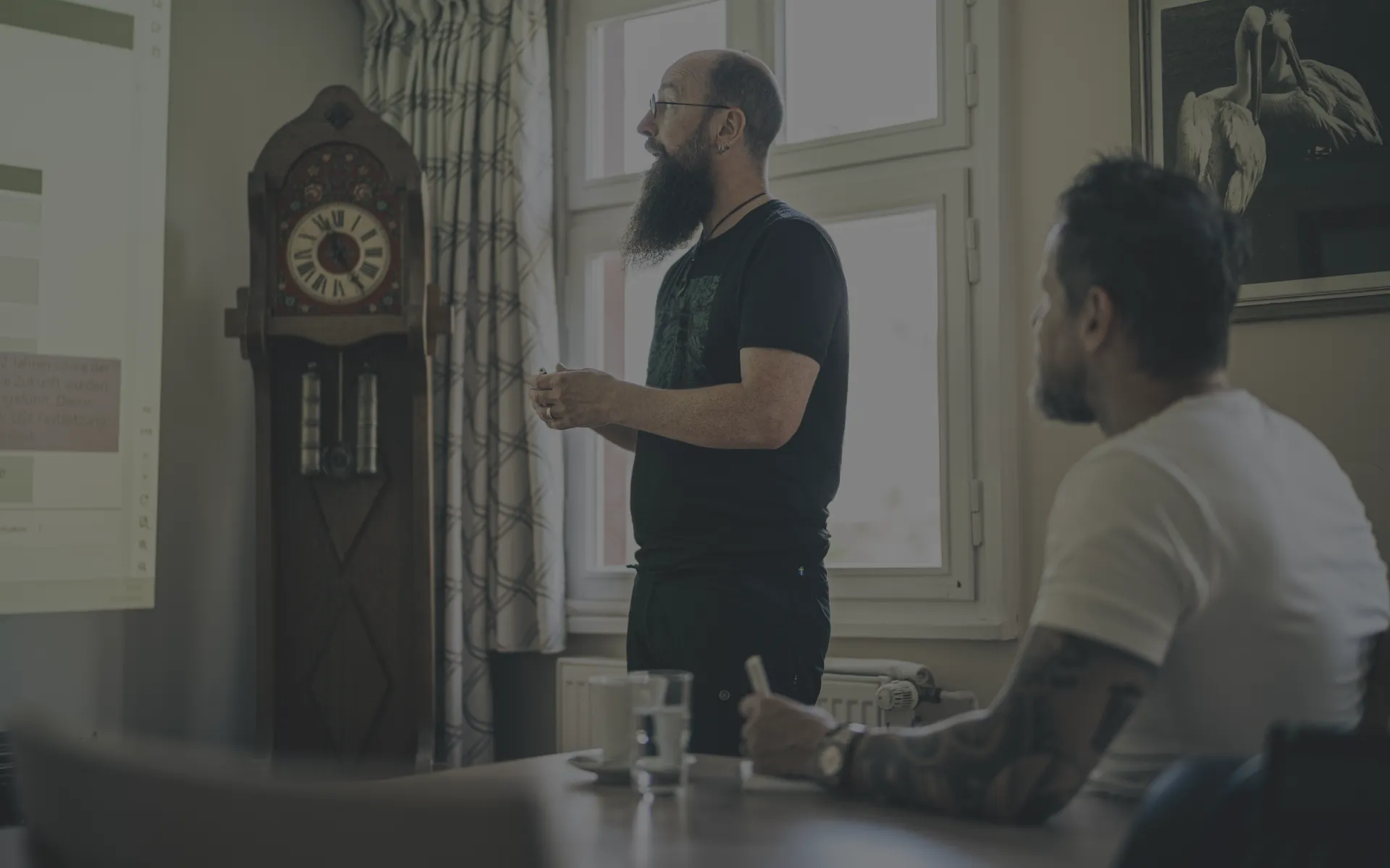 Teambesprechung vor einer Leinwand in lockerer Kleidung und Einrichtung mit alter Standuhr.