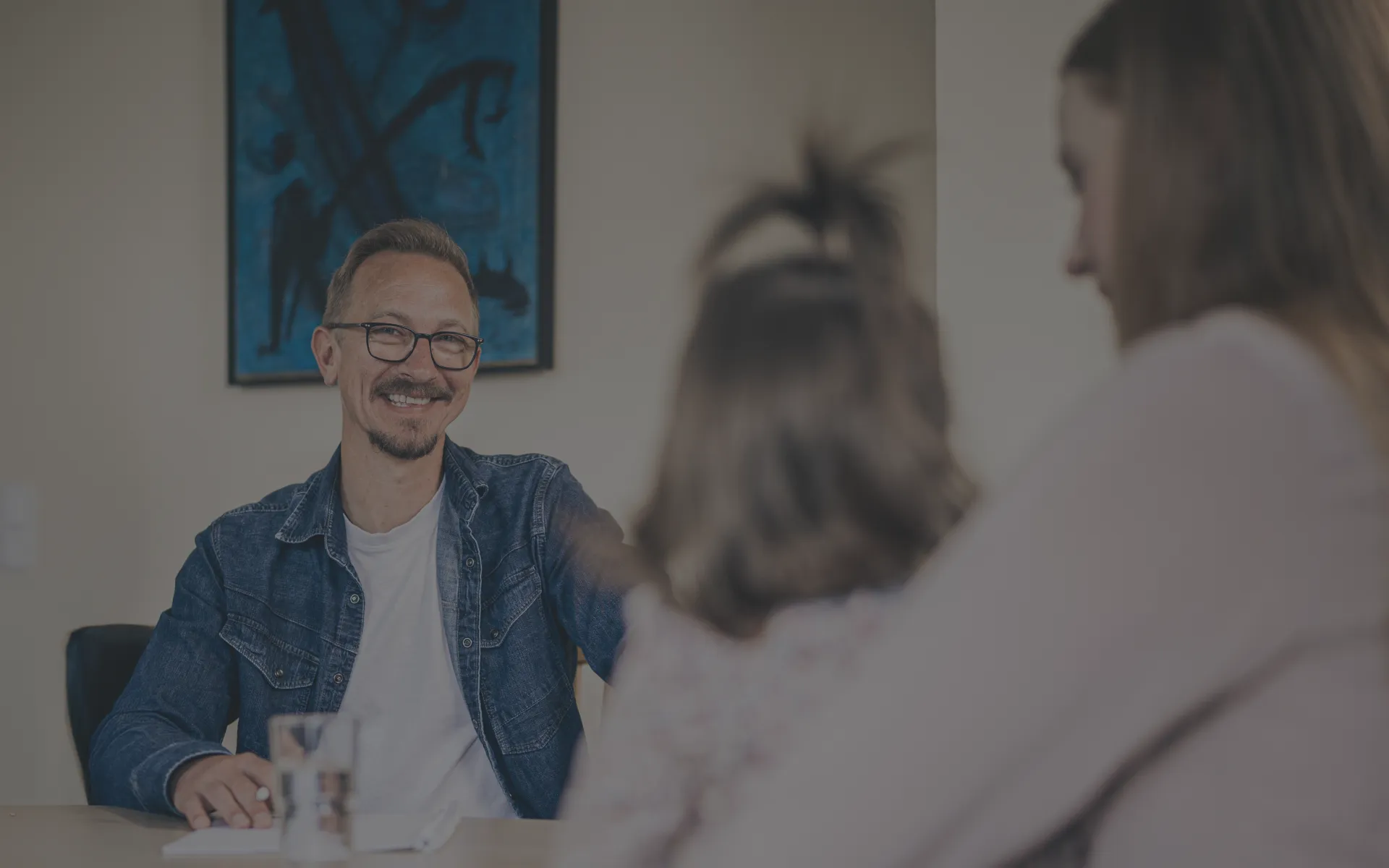 Herr Espey führt ein Kundengespräch mit einer Mama, die ihre kleine Tochter auf dem Schoß hält.