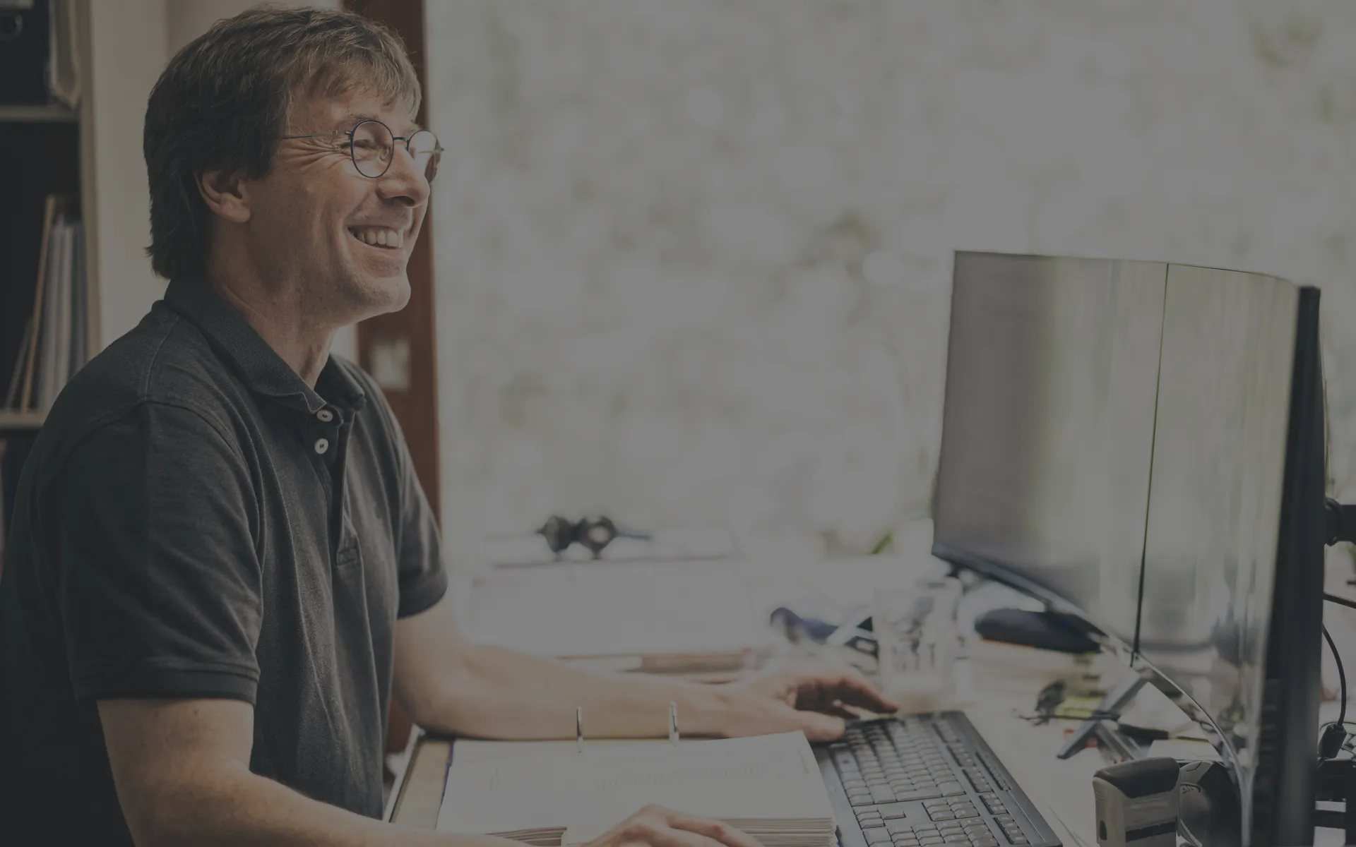 Ein Steuerberater sitzt lächelnd an seinem Arbeitsplatz und schaut auf einen Monitor.