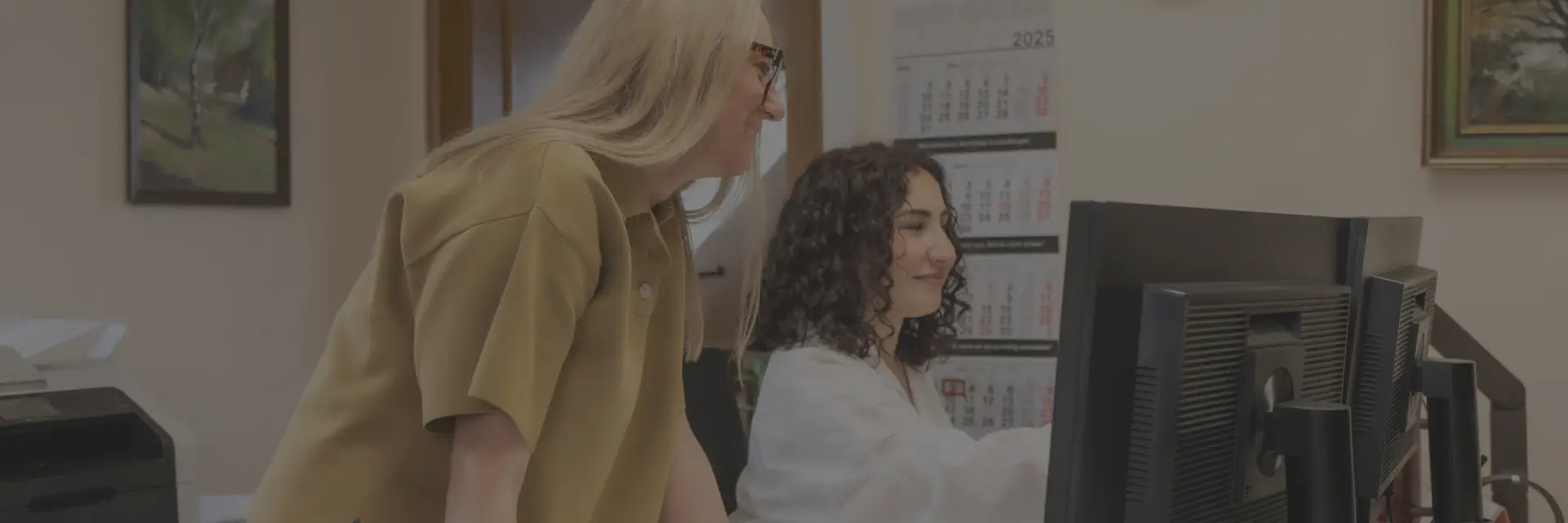 Zwei Kolleginnen besprechen etwas, das was auf einem Monitor zu sehen ist.